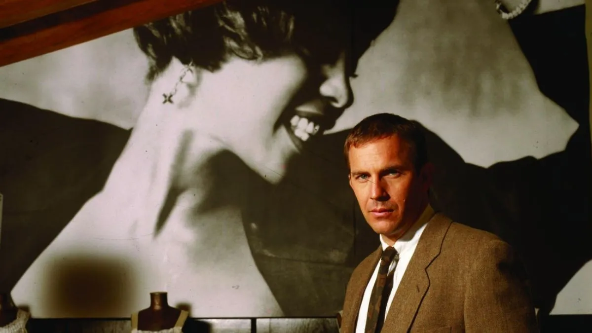 Kevin Costner in The Bodyguard with a picture of Whitney Houston behind