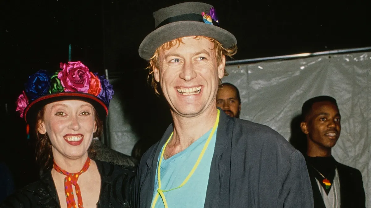 American actress Shelley Duvall, wearing a black jacket with a red neckerchief with multi-coloured polka dots and a floral trimmed hat, and American singer, songwriter and musician Dan Gilroy, who wears a black jacket over a turquoise blue t-shirt with a grey hat