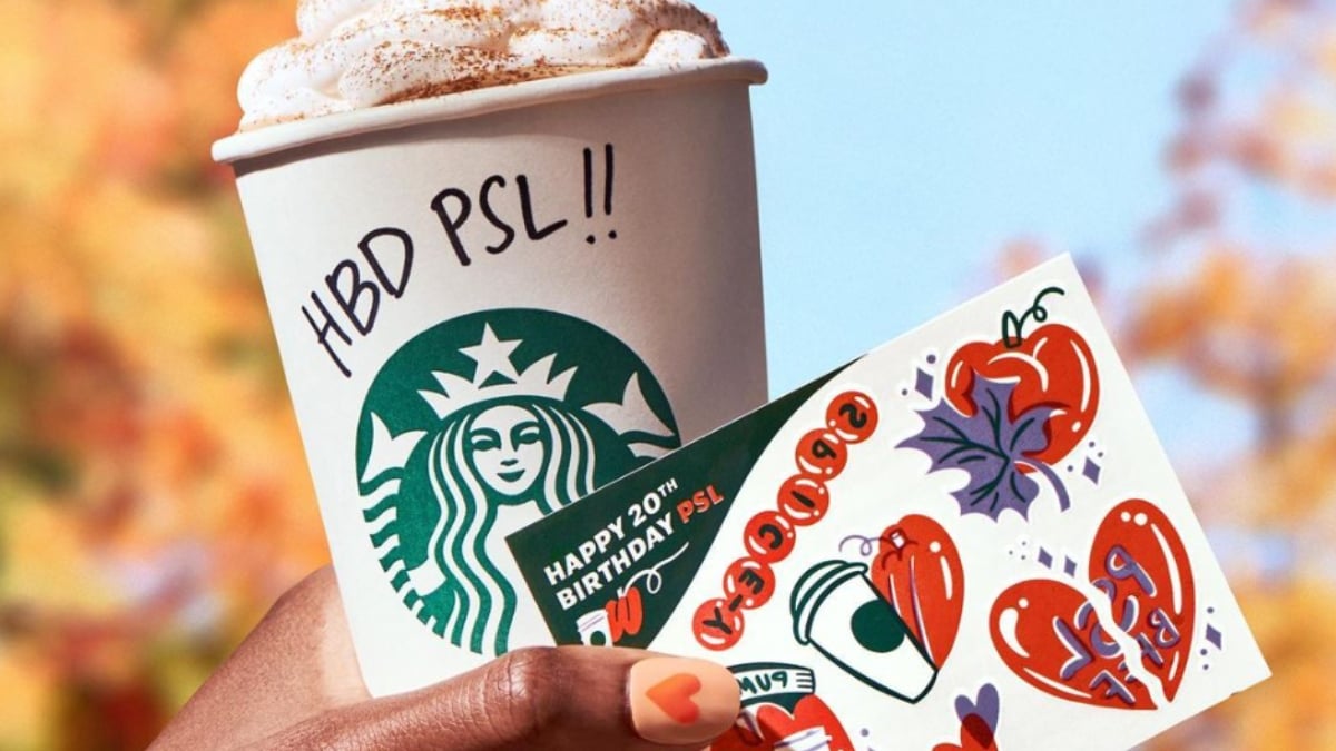 A hand holding a pumpkin spiced latte and a gift card from Starbucks