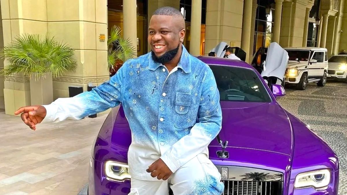 A picture of Ramon Olorunwa Abbas, aka Hushpuppi leaning against the hood of a car, smiling