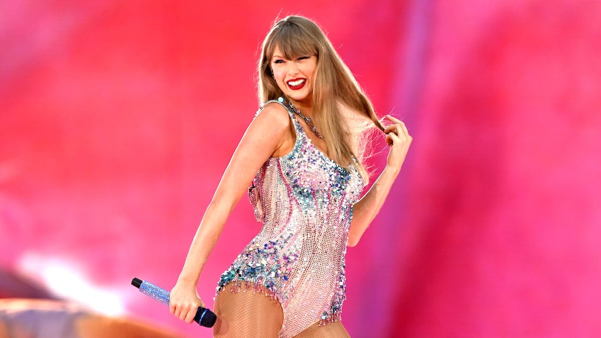 Taylor Swift smiling on the Eras Tour against a pink backdrop