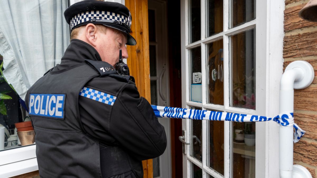 A policeman putting barricade tape across an elderly person's doorway. Stockphoto.