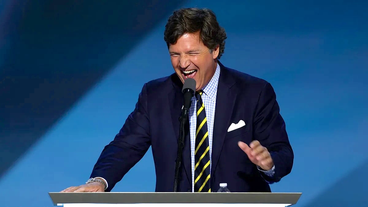 Tucker Carlson laughs ghoulishly at a podium