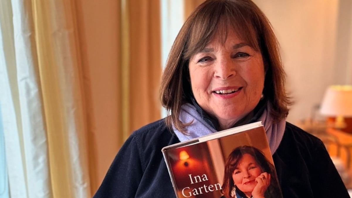 Ina Garten smiling and holding up a copy of her book