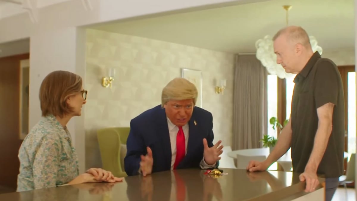 An actor portraying Donald Trump sits at a kitchen table with concerned Americans