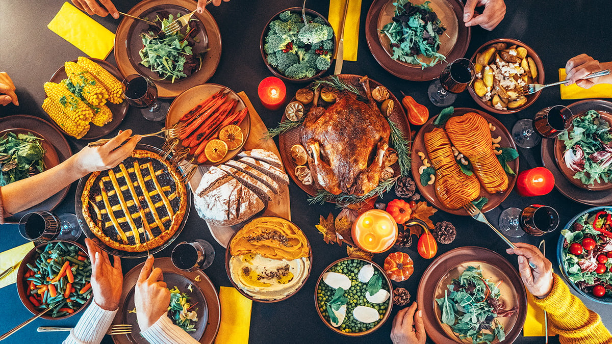 A spread of Thanksgiving food with eager hands cutting digging in