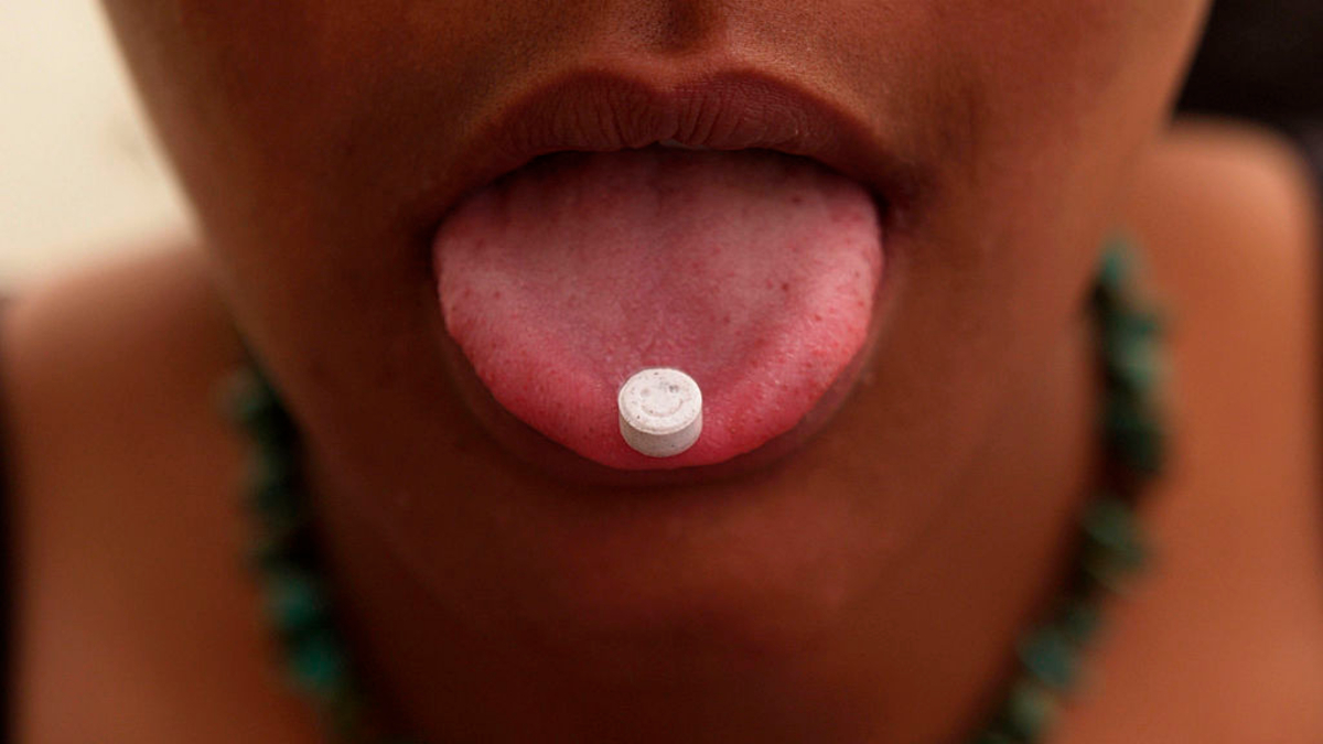 Girl with an ecstasy tablet on her tongue, smiley faced pill, UK 2004 