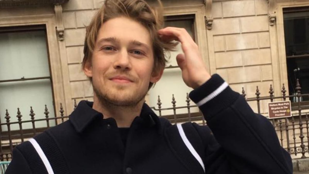 Joe Alwyn smiling and sitting outside