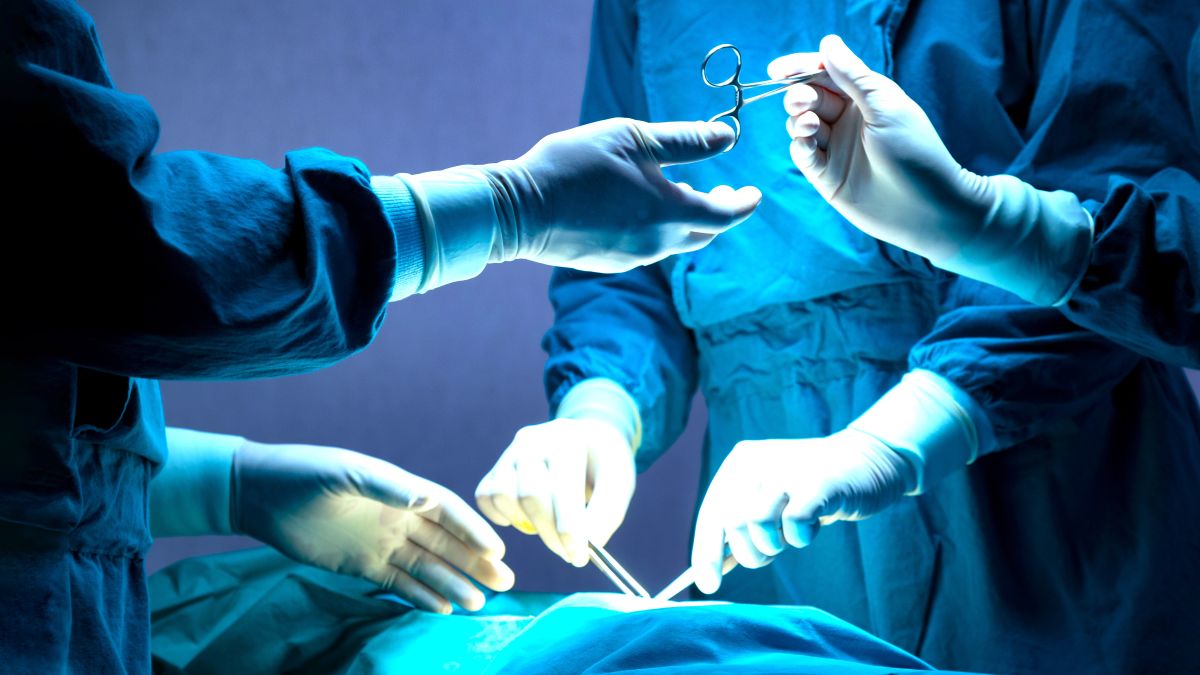 doctor and nurse medical team are performing surgical operation at emergency room in hospital. assistant hands out scissor and instruments to surgeons during operation.