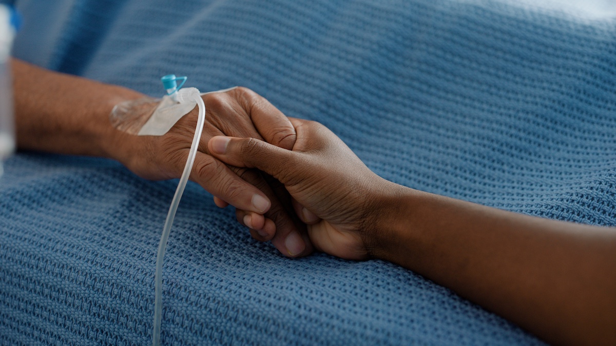 Hospital, holding hands and bed with trust, support and care together in a clinic after surgery. Senior, healthcare and cancer patient with empathy, kindness and caregiver with compassion with help