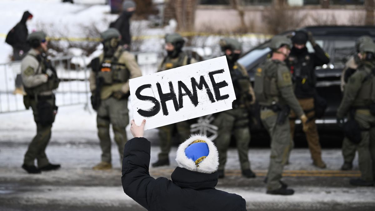 An onlooker holds a sign that reads "Shame" as members of law enforcement work the scene following a suspected shooting by an ICE agent during federal law enforcement operations on January 07, 2026 in Minneapolis, Minnesota. According to federal officials, the agent, “fearing for his life” killed a woman during a confrontation in south Minneapolis. (Photo by Stephen Maturen/Getty Images)