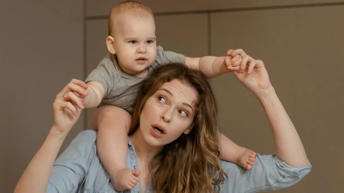 A joyful moment of mother carrying her baby on shoulders indoors, capturing love and bonding.