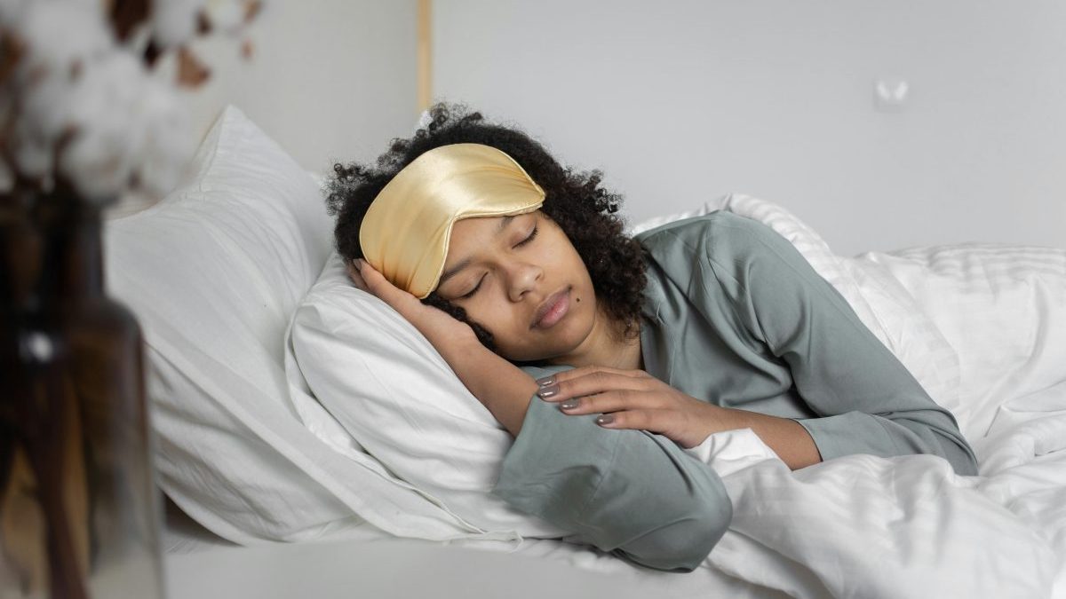 A young woman peacefully sleeps with a sleep mask, nestled in cozy white bedding.
