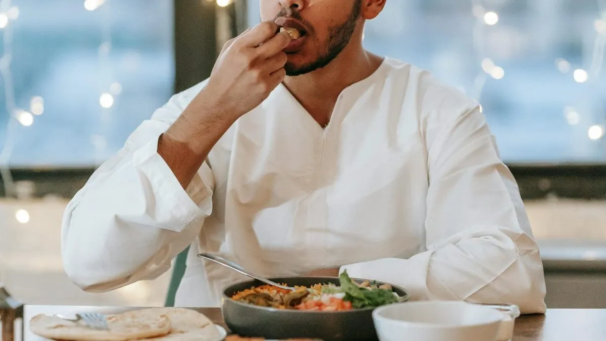 A Muslim man in a thobe enjoys a traditional iftar meal indoors, showcasing cultural dining customs.