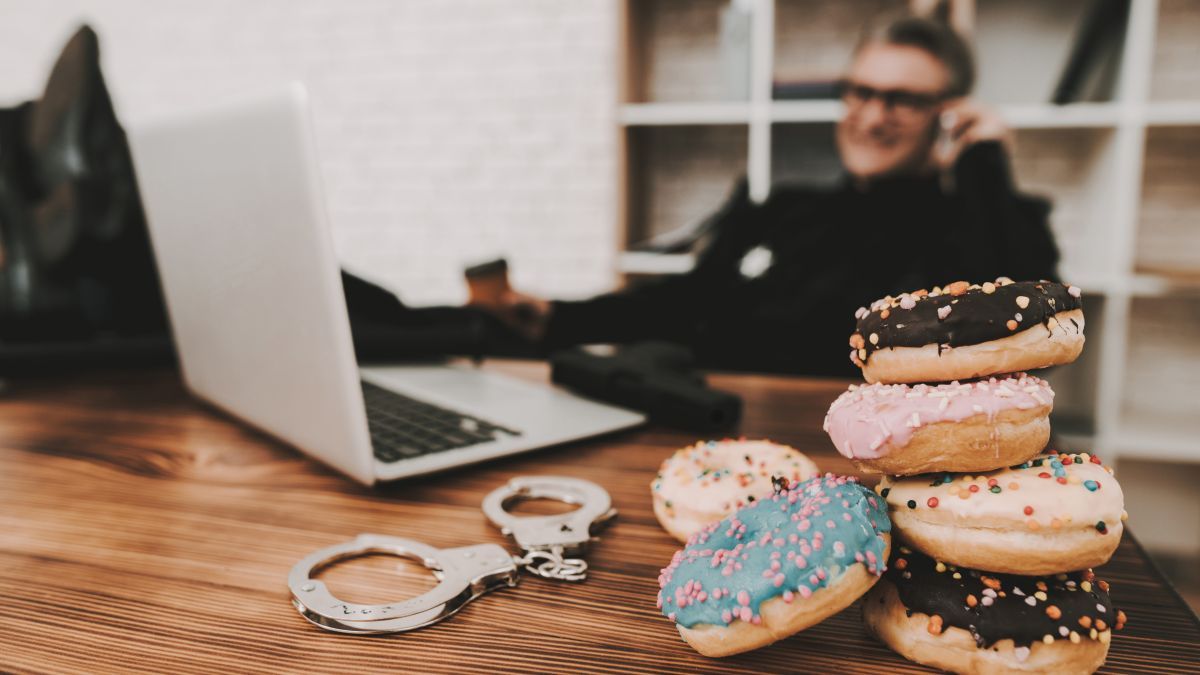 Smiling Policeman In Department Office. Relaxing Concept. Coffee Break. Cop's Donuts. Working Together. Citizen's Protection. Public Order. Phone Talking. Handscuffs On Table. Detective Uniform.