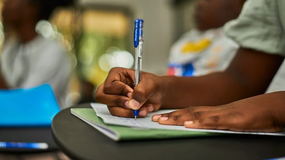 Focused hand writing in notepad during a classroom study session.