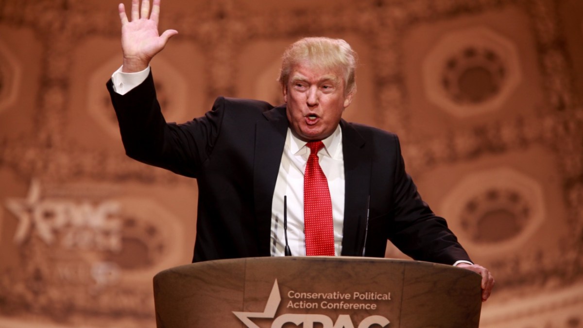 Donald Trump speaking at a podium with his hand raised